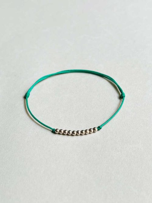 Gros plan posé devant un fond blanc le bracelet cordon Perles avec une rangée de 10 perles en argent et un cordon vert