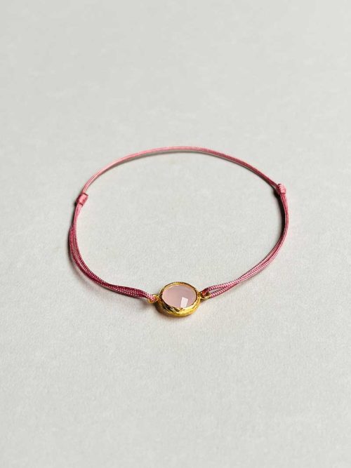 Gros plan posé devant un fond blanc le bracelet cordon Pierre Rose avec une pierre semi précieuse de quartz rose cerclée de plaqué or et un cordon vieux rose