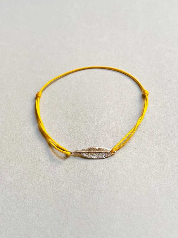 Gros plan posé devant un fond blanc le bracelet cordon Plume avec une plume en argent et un cordon jaune