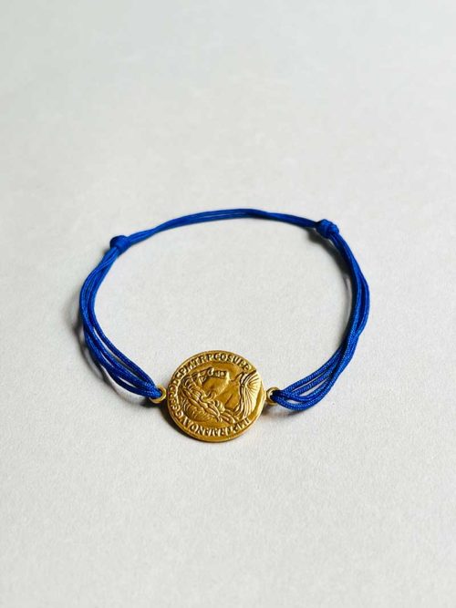 Gros plan posé devant un fond blanc le bracelet cordon Romane avec une pièce romaine en plaqué or et un double cordon bleu roi
