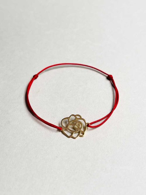 Gros plan posé devant un fond blanc le bracelet cordon Rose Doré avec une rose ajourée en plaqué or et un cordon prune
