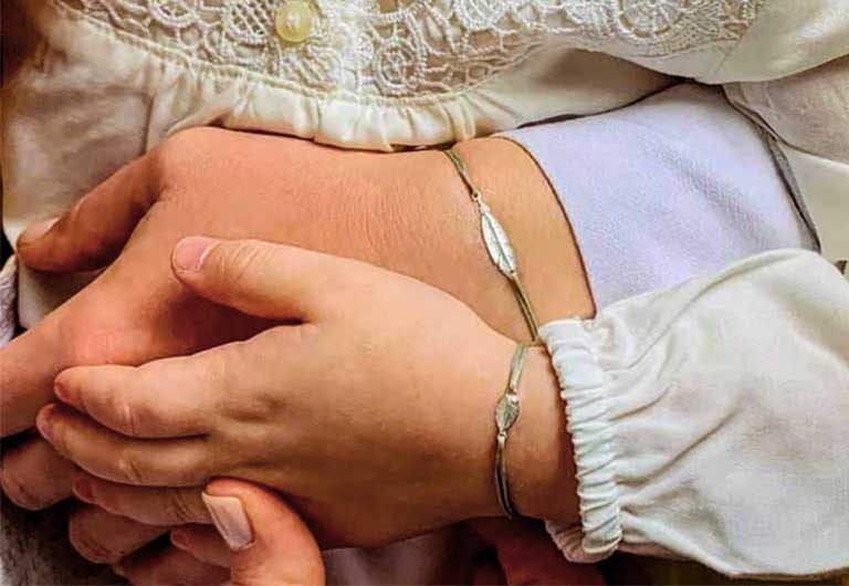 Vue de face une petite fille dans les bras de sa mère au poignet le même bracelet cordon Plume et Petite Plume en argent